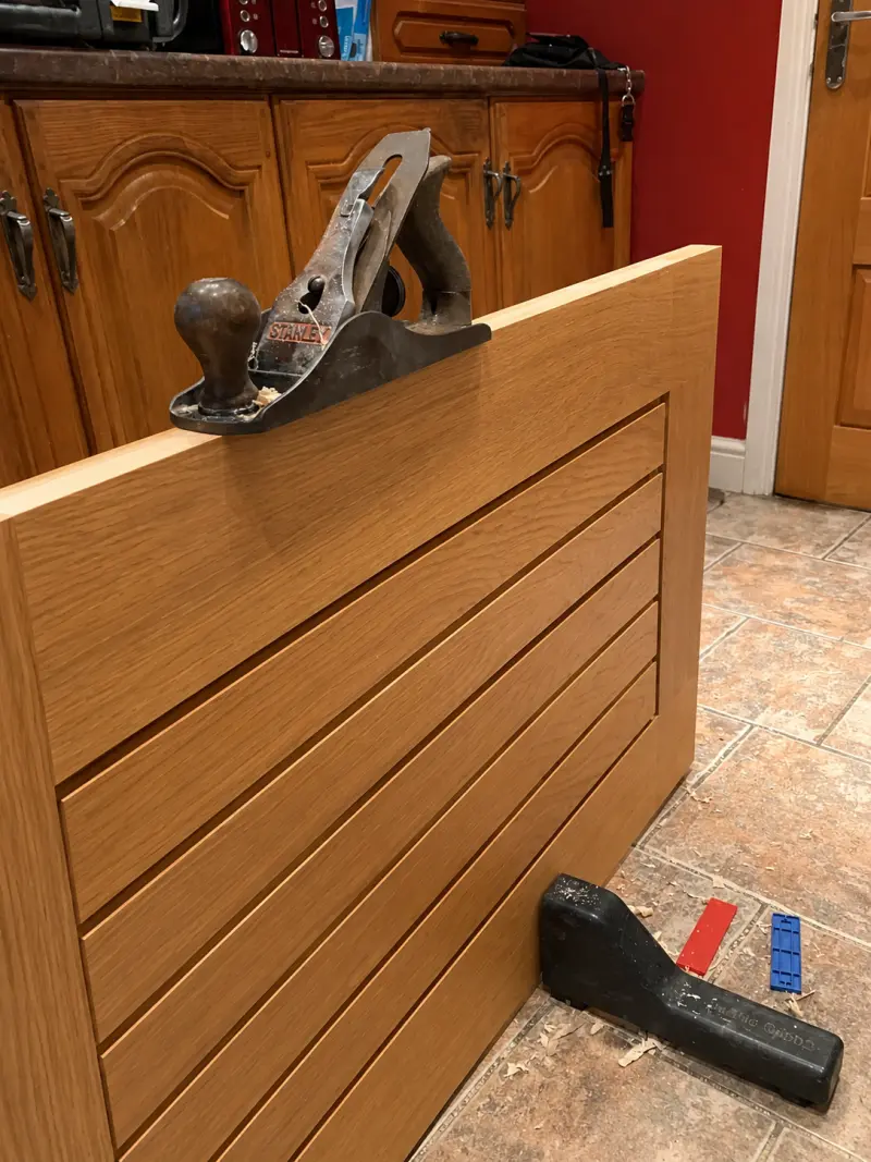 Carpenter planing the edge of an oak internal door during adjustment and repair